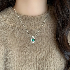 Silver necklace with green oval gemstone pendant and pavé stones on brown sweater