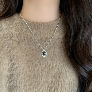 Elegant silver necklace with oval black onyx pendant worn over a brown sweater