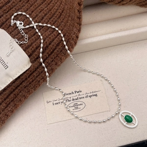 Close-up of vintage silver bead chain with oval openwork pendant and green gemstone