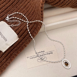 Detail of silver chain with tiger eye stone pendant on brown knit sweater texture