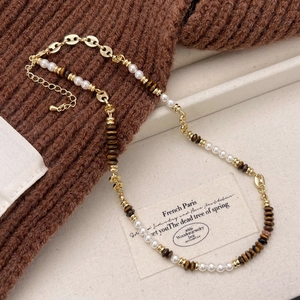 Vintage necklace with brown tiger eye beads and pearls over a brown sweater background