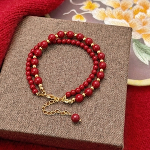 Détail d'un bracelet double rang de perles rouges et accents dorés sur son coffret