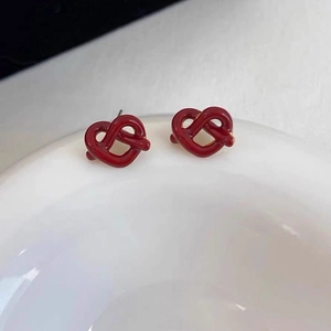 Detailed view of red heart knot stud earrings with glossy enamel on a white plate