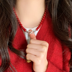Detalle de collar de cuentas rojas con un colgante infinito de plata en una modelo
