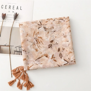 Detailed close-up of beige cotton scarf with abstract floral prints and tassel fringe
