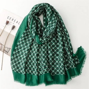 Green cotton scarf with geometric floral print and frayed edges on a white tabletop