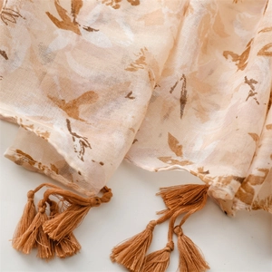 Detail of light beige cotton-linen scarf with brown floral pattern and tassel trim