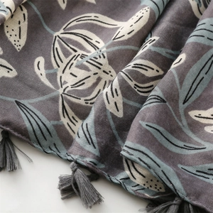 Détail d'écharpe fleurie gris-violet avec feuilles crème et bordure à pompons gris