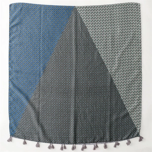 Detail of geometric patchwork scarf showing blue diamond patterns and grey tassels
