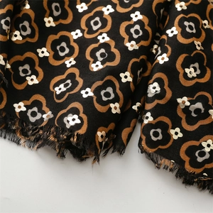 Detail of black scarf with golden camellia floral patterns and fringed edges