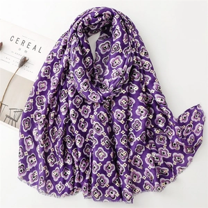 Macro shot of dark purple scarf with floral pattern and soft frayed edges over a white desk