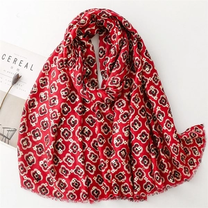 Detail of red floral scarf with gold foil accents and frayed edges on white background