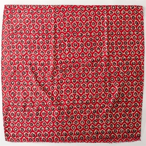 Detail of red square scarf featuring black floral patterns and raw fringe edge textures