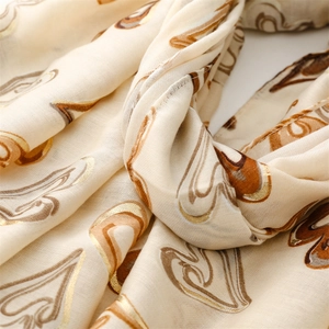 Vue détaillée d'une écharpe crème avec motifs paisley dorés et texture de tissu doux