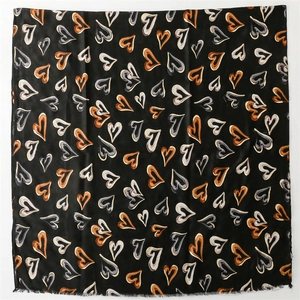 Détail d'une écharpe carrée noire avec motifs de cœurs abstraits et bords effilochés