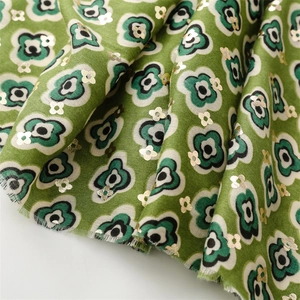 Macro detail of grass green fabric with black flower prints and golden foil texture