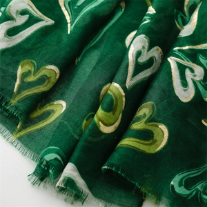 Détail d'une écharpe en coton vert foncé avec motifs cœurs dorés et bords effilés