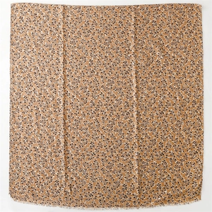 Close-up of camel cotton-linen scarf with black foliage print and frayed fringe edges
