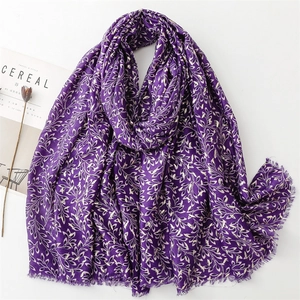 Detail of deep purple scarf featuring golden leaf prints and fringed edges on white
