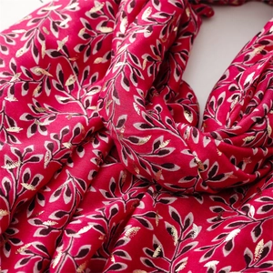 Close-up of red scarf with golden foil leaf patterns and rich textile texture