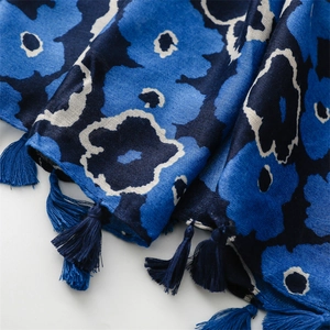Detailed close-up of blue floral scarf texture with elegant fringe tassels on the edge