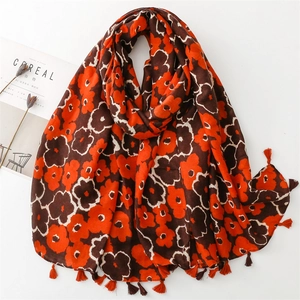 Close-up of vibrant orange floral print scarf with tassel trim and lifestyle props