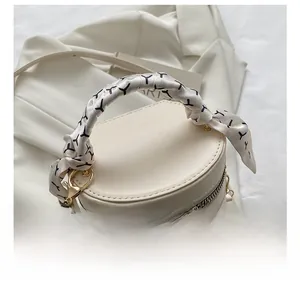 Detail of cream barrel bag with elegant silk scarf wrapped handle and gold hardware