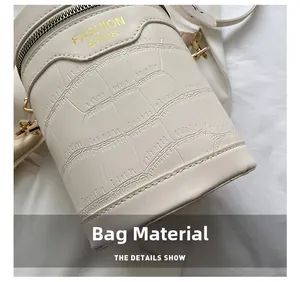 Detail showing white crocodile pattern texture and golden logo on cylindrical bucket bag