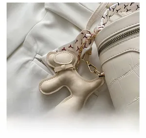 Detail view of cream bucket bag with crocodile texture, puppy charm and floral scarf