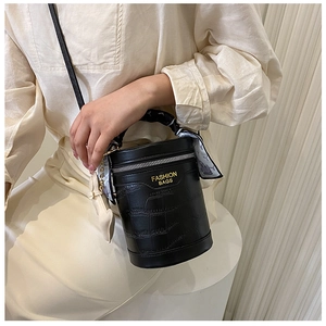 Detail of black crocodile texture cylinder bag with silk scarf handle and leather strap