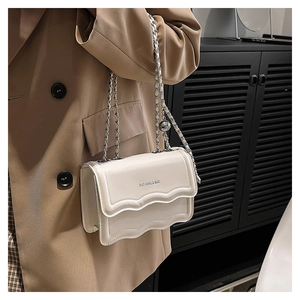 Detail of off-white crossbody bag with wavy edge flap and silver chain on model
