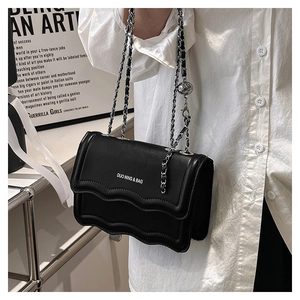 Detail of black crossbody bag with wave-edge flap and silver metal chain strap