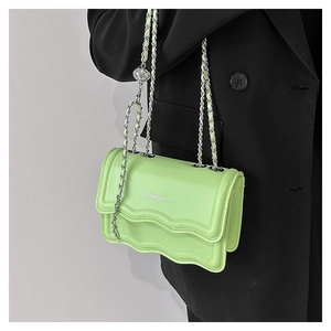 Detail of green leather bag featuring wavy edge flap and silver chain with metallic ball