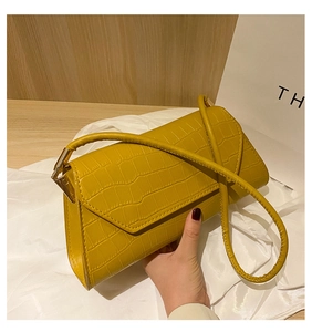 Close-up of bright yellow crocodile pattern handbag held by hand on wooden surface