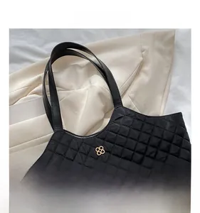 Macro view of black quilted tote bag with golden floral metal logo and refined texture