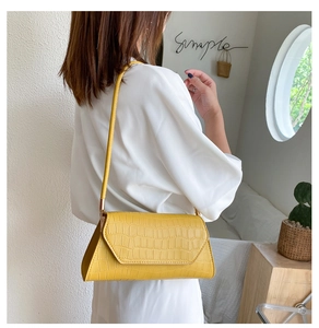 Detail of yellow crocodile pattern baguette bag worn over shoulder in minimalist setting