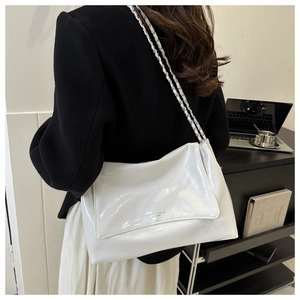 Sac à épaule en cuir verni blanc brillant avec chaîne argentée porté par un modèle