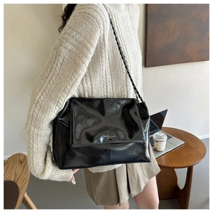 Détail d'un sac cabas en cuir verni noir avec bandoulière chaîne dans un café chaleureux