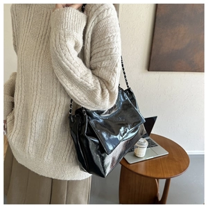 Gros plan d'un sac à bandoulière en cuir verni noir avec chaîne argentée sur un modèle