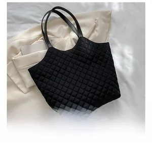 Size comparison of a black quilted tote bag with a mobile phone on a beige blazer