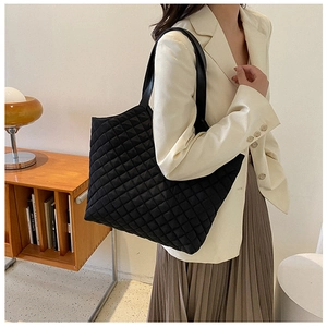 Detail of a large black quilted tote bag with a leather shoulder strap for casual wear