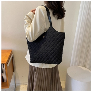 Detail of black quilted tote bag with diamond pattern and golden logo in office setting