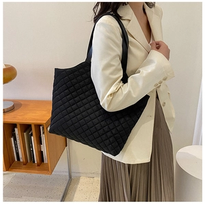 Quilted black tote bag with diamond stitching shown on model in minimalist interior