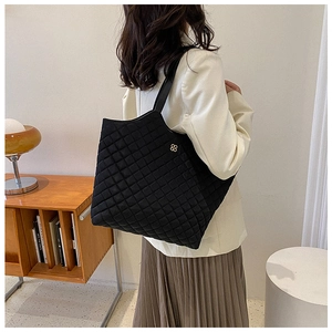 Detail of black quilted tote bag featuring a golden clover logo on a nylon shoulder bag