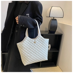 Close-up of white quilted tote bag with glossy finish and clover metal charm