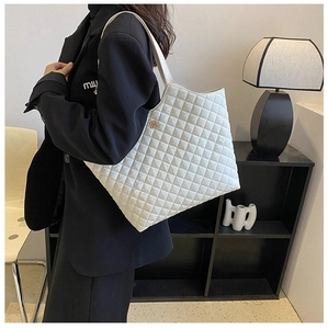 Close-up of white quilted tote bag with gold clover charm and diamond stitching