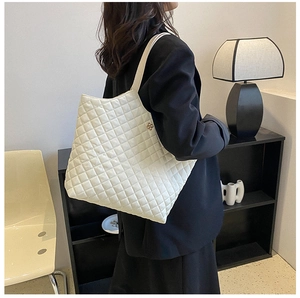 Detail view of cream tote bag featuring quilted diamond texture and golden floral charm