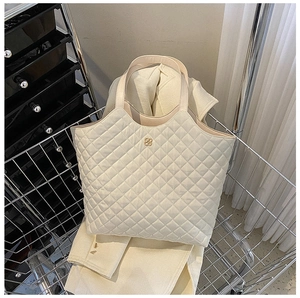 Detail of a creamy white quilted tote bag with a golden four-leaf clover metal buckle