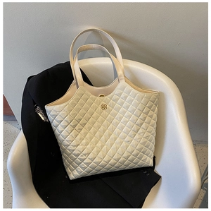 Close-up of quilted cream tote bag featuring a gold clover emblem on a chair