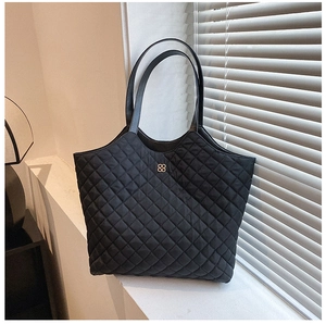 Detail of black quilted tote bag with golden clover logo on a white windowsill